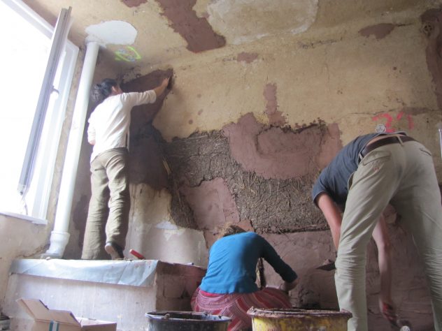 Drei Personen füllen neuen Lehm in Lücken eine alten Lehmwand