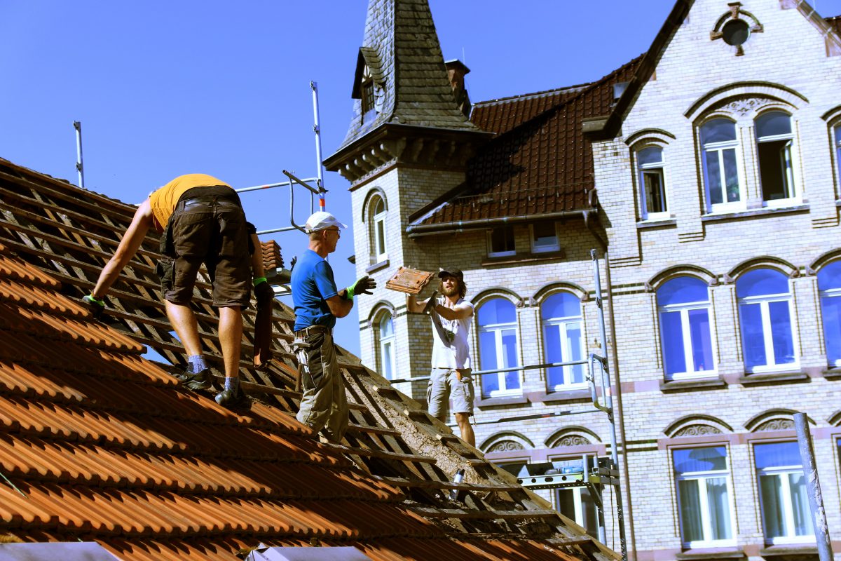 Dacharbeiter wirft einem Helfer einen Dachziegel zu